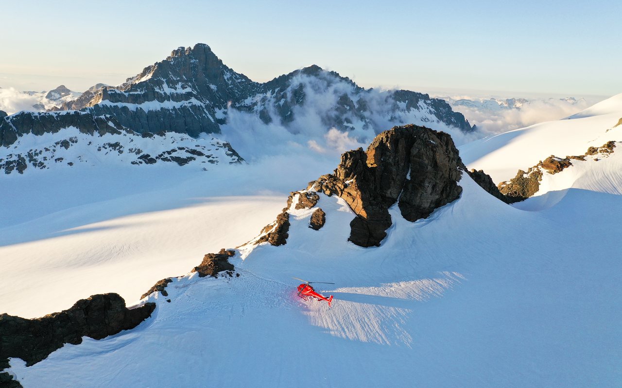 Verschneiter Bergkamm aus der Luft, davor ein roter Helikopter