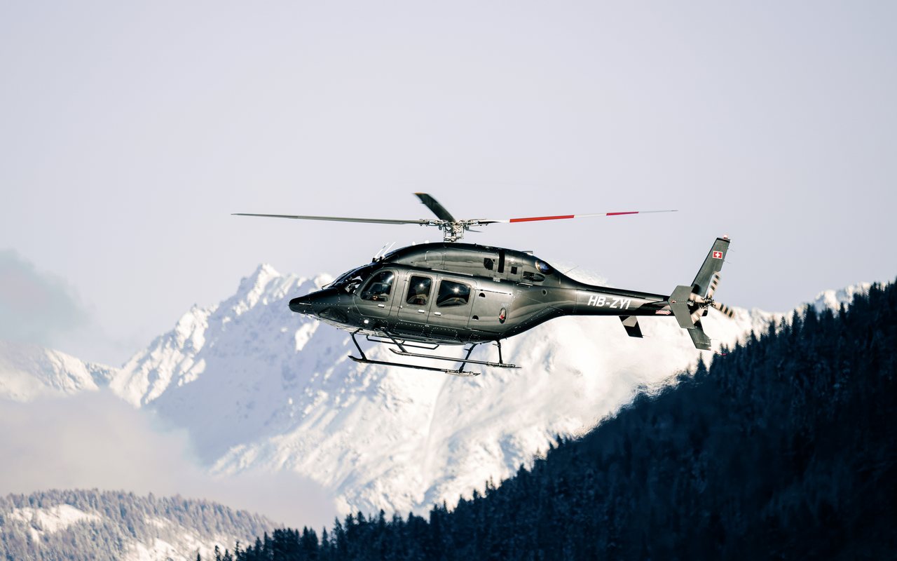Bell 429 der Airport Helicopter AHB AG im Flug über bewaldeten Berghängen