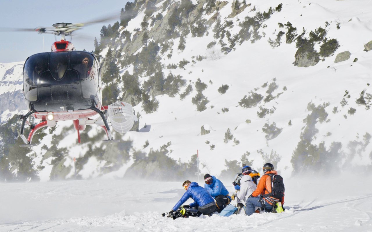 Skifahrer mit Ausrüstung im Schnee, dahinter ein Helikopter der Airport Helicopter AHB AG