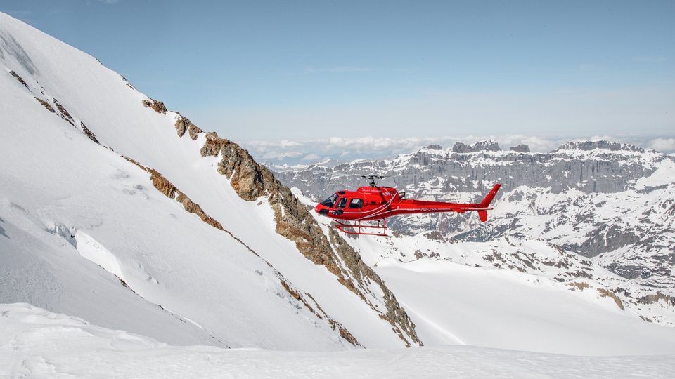Roter Helikopter im Flug über einem verschneiten Grat im Hochgebirge
