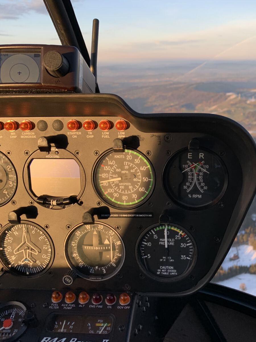 Blick aus dem Cockpit eines Robinson R44 im Flug über der Voralpenlandschaft im Abendlicht